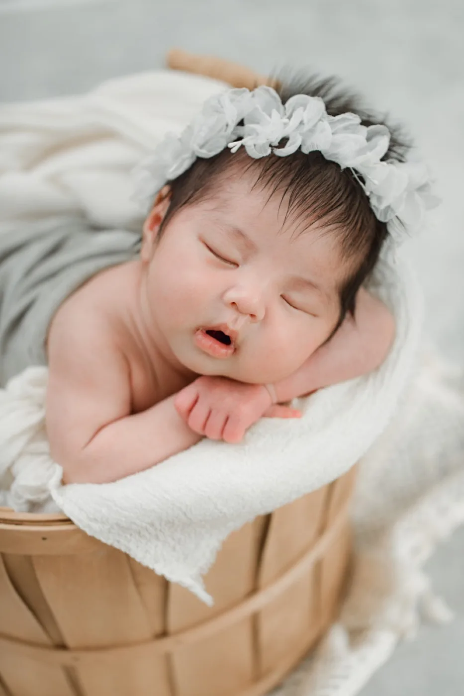 チュールの帽子をかぶり、かごの中で頬に手を添えて眠る新生児