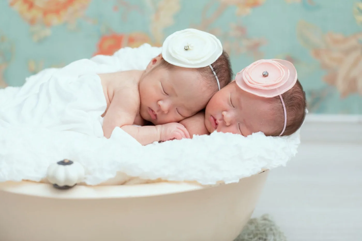ベビーバスの中で頬を寄せ合って眠る双子の新生児
