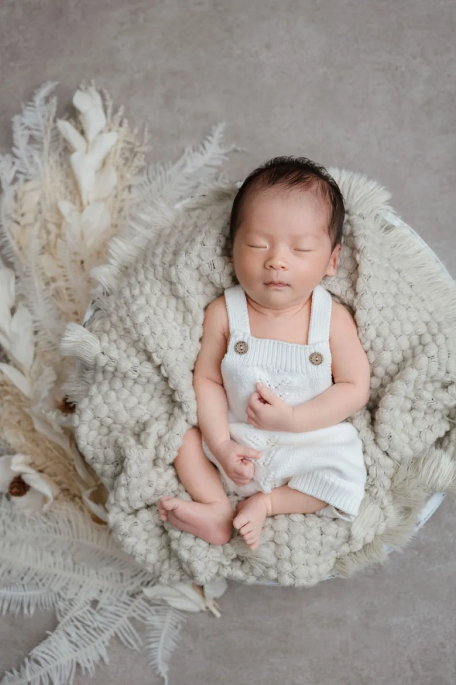 白いニットのロンパースを着て、かごの中で眠る新生児