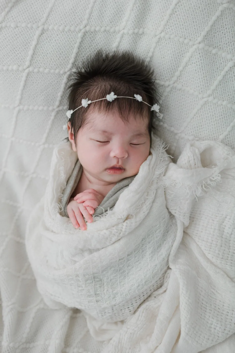 白い花冠をつけ、白いおくるみに包まれて眠る新生児