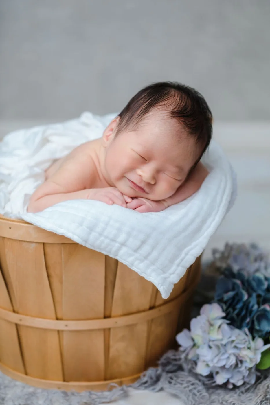 木のかごのふちに頬をのせて眠る新生児