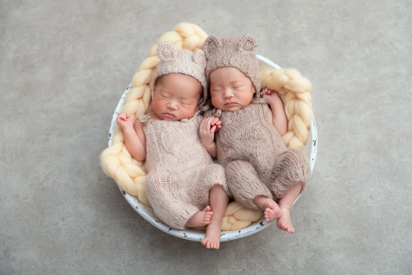 くまの帽子とニットの衣装で、かごの中に並んで眠る双子の新生児