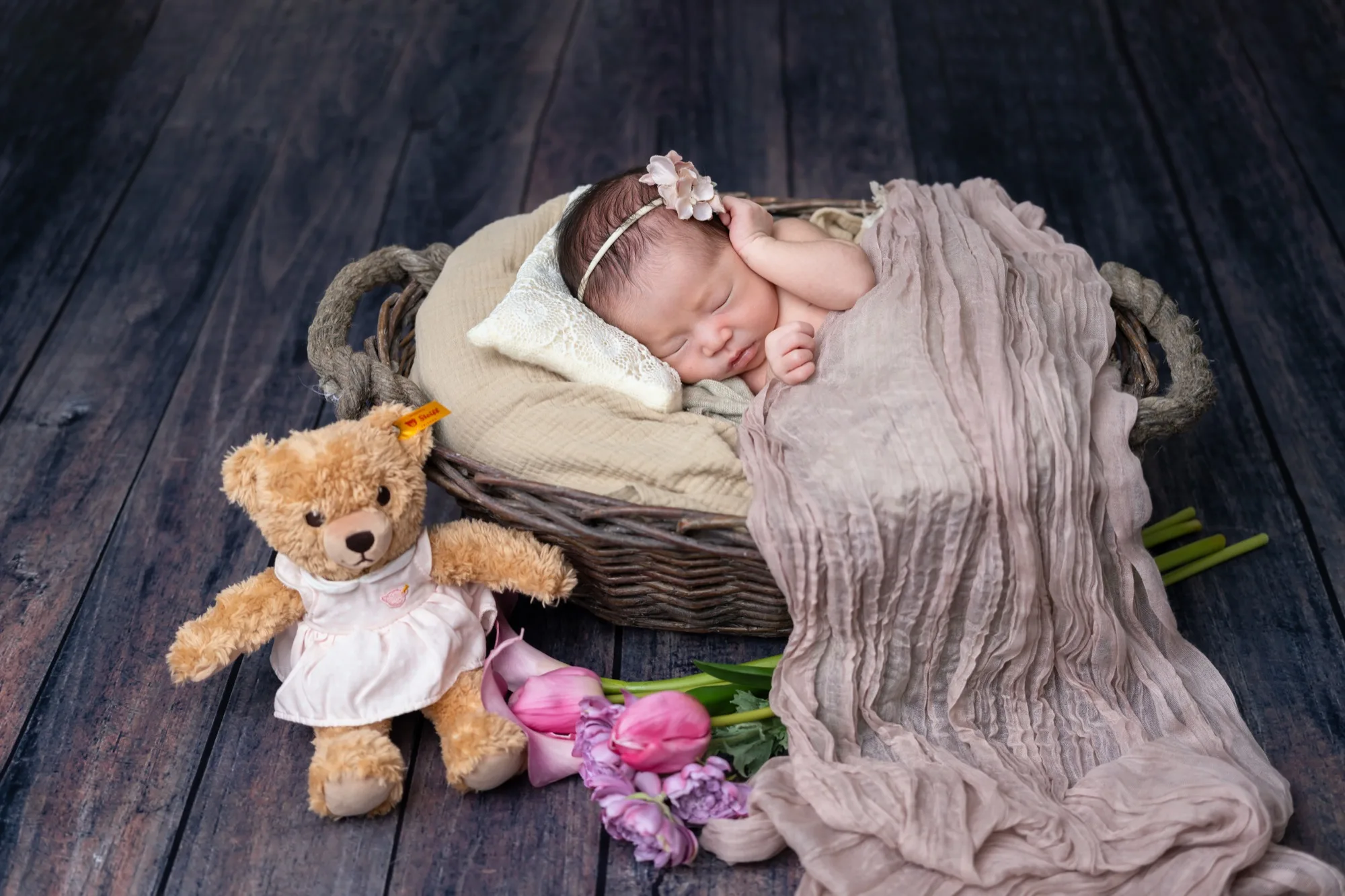 テディベアとチューリップを添えた、かごの中で眠る新生児