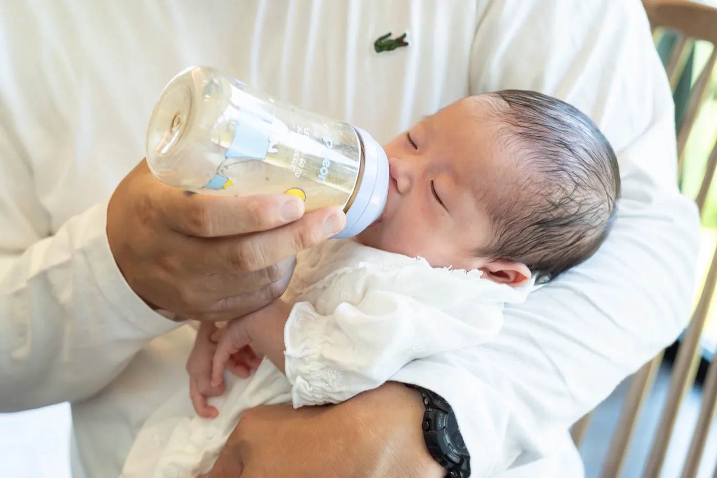 父親の腕に抱かれて哺乳瓶からミルクを飲む、生まれたばかりの赤ちゃん