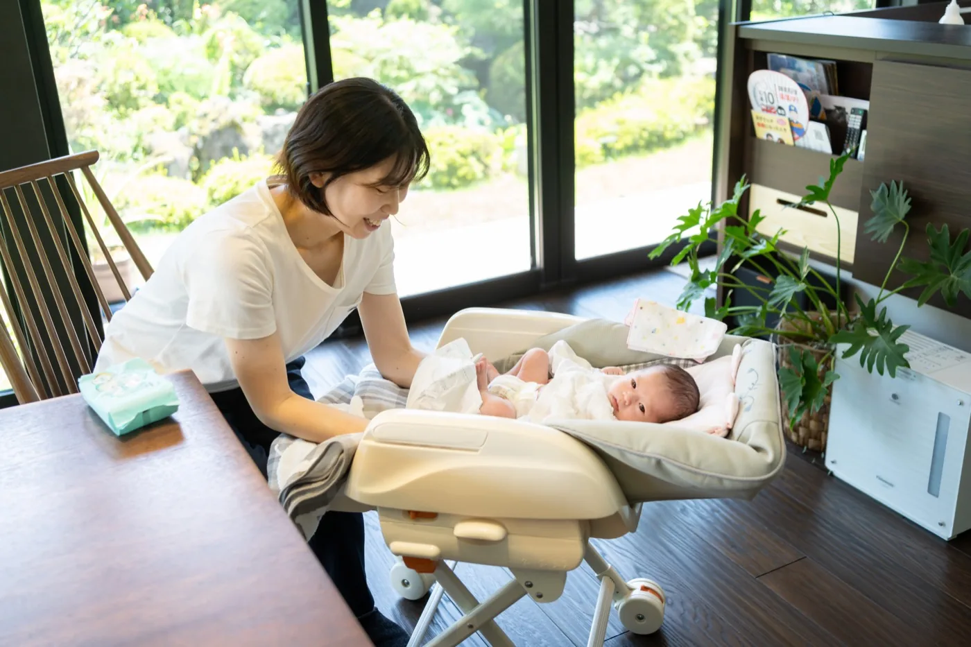 自宅のリビングで、ベビーベッドの赤ちゃんのおむつを替える母親