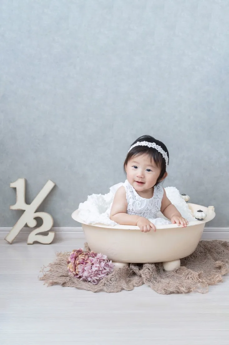 ベビーバスに座って笑う生後6か月の赤ちゃん。となりに1/2の文字