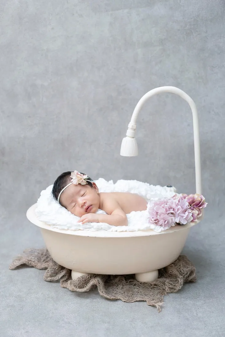 ベビーバスの中で眠る新生児。シャワーの飾りと花を添えて