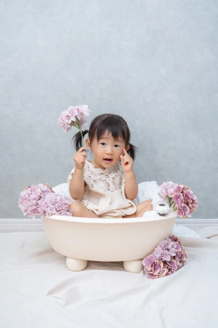 ベビーバスに座り、花を手にした1歳の子ども