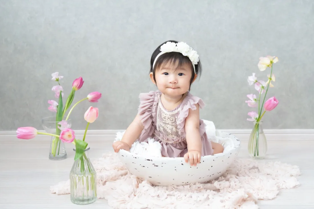白い器に座って笑う生後6か月の赤ちゃん。まわりにチューリップ